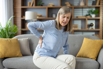 Unhealthy mature woman keeping hand on back while struggling with pain in spinal bones. Ill female...