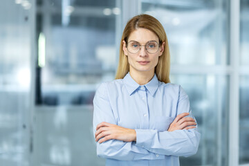 Fototapeta premium Serious ceo of financial company standing with arms crossed on chest and feeling proud about job success. Millennial female waiting for formal business meeting with investors in boarding room.