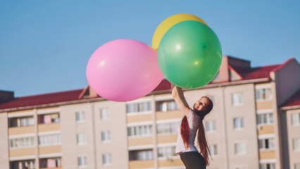 A girl happily poses with large with colorful balloons in the city.