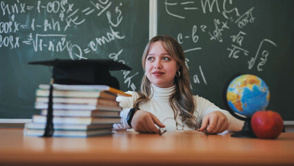 A schoolgirl wearing glasses poses against a background of books, an apple, a globe and a...