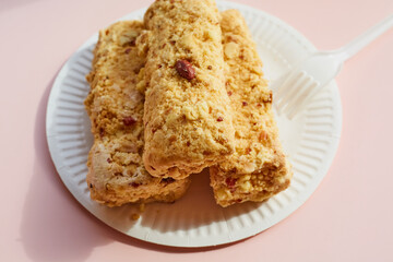 Creamy cake with nuts on a paper plate with a plastic fork on a pink background, nut dessert on disposable dishes, a portion of cake with nuts