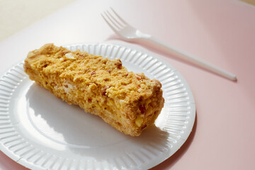 Creamy cake with nuts on a paper plate with a plastic fork on a pink background, dessert on disposable dishes