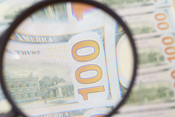 Magnifying glass enlarges the figure one hundred on dollar bills, search for forgery, counterfeit money, increase in profit