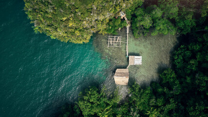 Drone, ocean and wood building in nature by beach, forest and woods with trees outdoor in Malaysia. Kelong, aerial view and house at sea for fishing, offshore or travel by water in summer environment