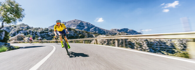 Obraz premium Mature Adult on a racing bike climbing the hill at mediterranean sea landscape coastal mountain road - mallorca mountains