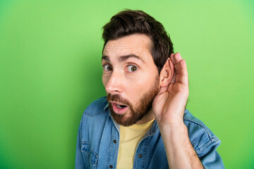 Photo of curious handsome guy wear denim jacket arm ear listening you empty space isolated green...