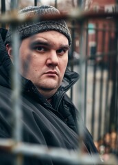 Portrait of a British scowling man behind a fence.