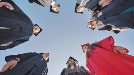 Graduates in robes stand in a circle. View from below.