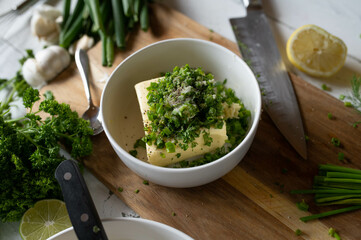 Making herb butter. Bowl with butter and fresh cut herbs,  such as chives, parsley, garlic, salt,...