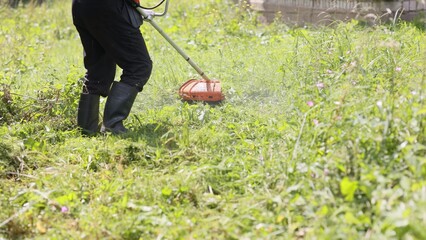 A man mows the grass with a trimmer on a summer day in the countryside.