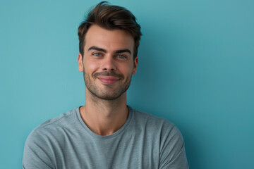 A man in a grey shirt is smiling in front of a blue wall