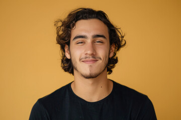 A young man with curly hair and a beard smiles for the camera