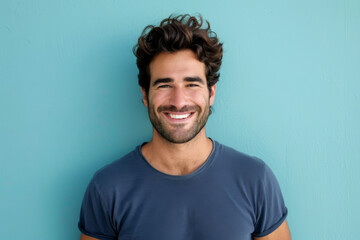 A man in a blue shirt is smiling in front of a blue wall