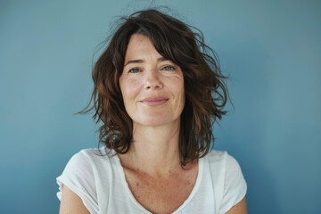 A woman in a white shirt smiles in front of a blue wall