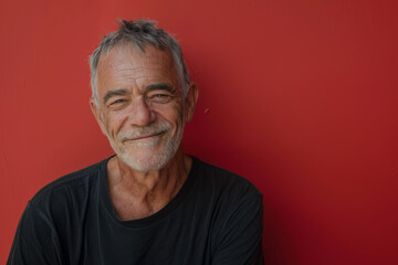 A man with gray hair and a beard is smiling in front of a red wall