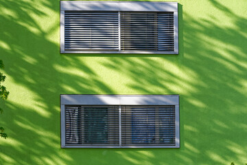 Close-up of green facade of apartment building with windows and shutters and silhouette of trees at Swiss City or Zürich. Photo taken April 18th, 2024, Zurich, Switzerland.