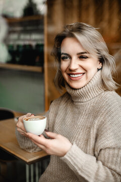Joyful Woman Relaxing with Coffee. A woman smiles warmly as she sits at a table with a cup of coffee, radiating contentment and relaxation while savoring her drink.