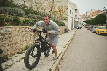 European young man pushing his electric mountain bike up the street. Active lifestyle. Sport....