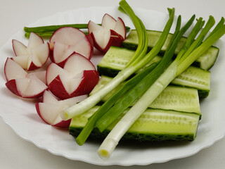 Fresh raw radishes, cucumbers and green onion are on a white plate
