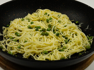  Italian spaghetti with green peas is sprinkling with grated parmesan cheese on the frying pan