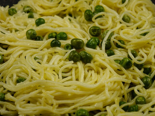 Italian spaghetti with green peas is sprinkling with grated parmesan cheese, background