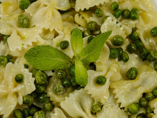 Italian Farfalle pasta with green peas and grated Parmesan cheese on a white plate, background