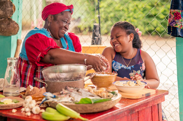 African-American mother teaches her little daughter how to cook Tapado, traditional Garifuna dish- Ingredients for Tapado on the kitchen table. Happy family in the kitchen.