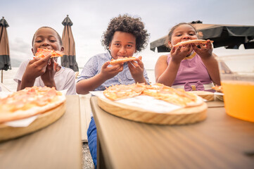 Group of African American boys and girl enjoying a delicious pizza in a restaurant. siblings...