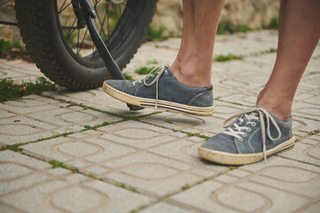 Cropped view male legs in denim sneakers near the electric bicycle wheel.