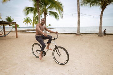 Portrait of a cheerful young African American man riding a bicycle on the shore of the beach...