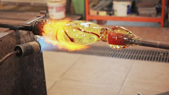 A close-up view of a glassblower's hands shaping molten glass into a delicate piece of art in Murano, Italy. Close up hand blown glass processing. Making glass in Murano Italy. 