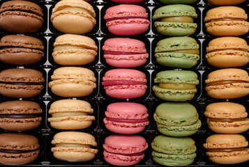 Multi-colored macarons in a plastic box, top view.