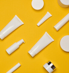 Various types of white plastic packaging, bottle, jar, tube on a yellow background.