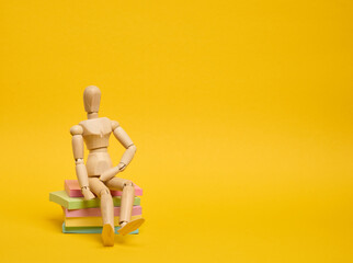 A wooden puppet doll sits on a stack of paper multi-colored stickers on a yellow background