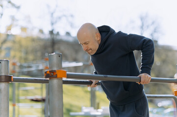 a man in sportswear works out in the open air with the help of parallel bars