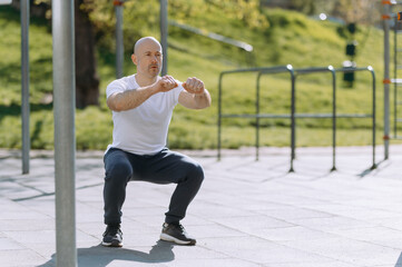 bald man squats down outdoors
