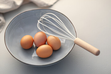 Four eggs and a whisk ready for use in a bowl for baking.