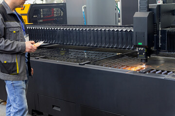 A worker operates a steel laser cutting machine at a factory