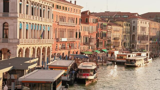 Venetian gondolier punting gondola through green canal waters of Venice Italy. Beautiful view of traditional Gondolas on famous Canal Grande in romantic golden evening light at sunset.