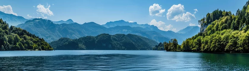 Tuinposter Serene landscape of a majestic mountain range by a tranquil blue lake with forested shores bathed in sunlight © Michal