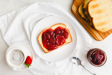 Breakfast with Toast and Strawberry Preserves and Cappuccino: Slice of toasted white bread and homemade berry preserves with coffee on white table