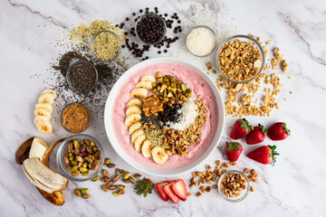 Strawberry Smoothie Bowl Loaded with Healthy Toppings: Fruit smoothy bowl with sliced banana, seeds, nuts, peanut butter, and dark chocolate chips
