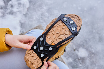 Pedestrian putting cleats on his shoes for extra traction during a winter walk during icy...