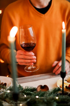 Man in orange sweater holding glass of red wine while celebrating Christmas with family at home