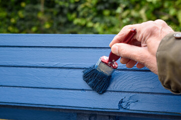 Male hand using a paint brush to paint onto a plank of wood