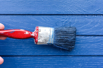 Paint brush painting blue paint onto a wooden surface