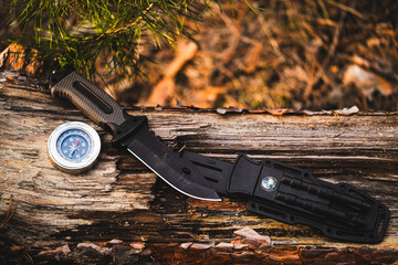 Hunting knife and compass on a log in the autumn forest.