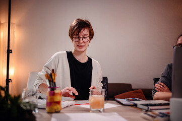 An artist examines her work with a critical eye, surrounded by the cozy glow of a studio lamp, indicative of the creative process