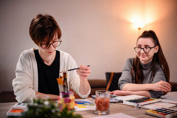 In a creative session, one artist paints while the other plans, a perfect example of collaborative effort and artistic consultation.