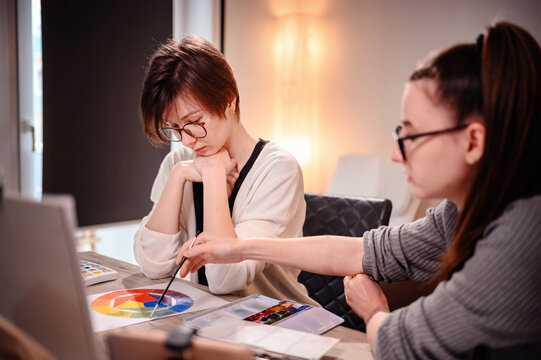 Artists in a dynamic brainstorm, one deep in thought and the other poised to implement ideas, in the warm ambiance of their studio